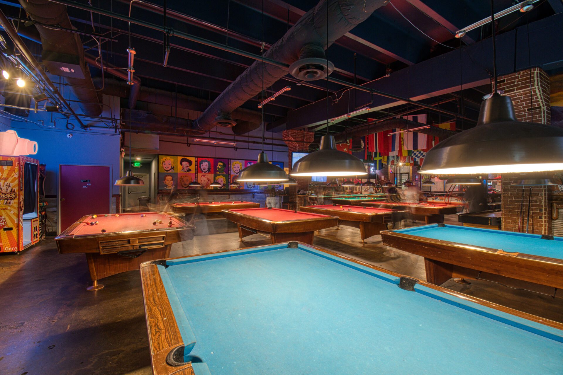 A pool table in an empty room with many tables.