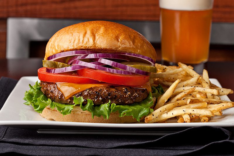 A hamburger and fries on a plate with a beer.