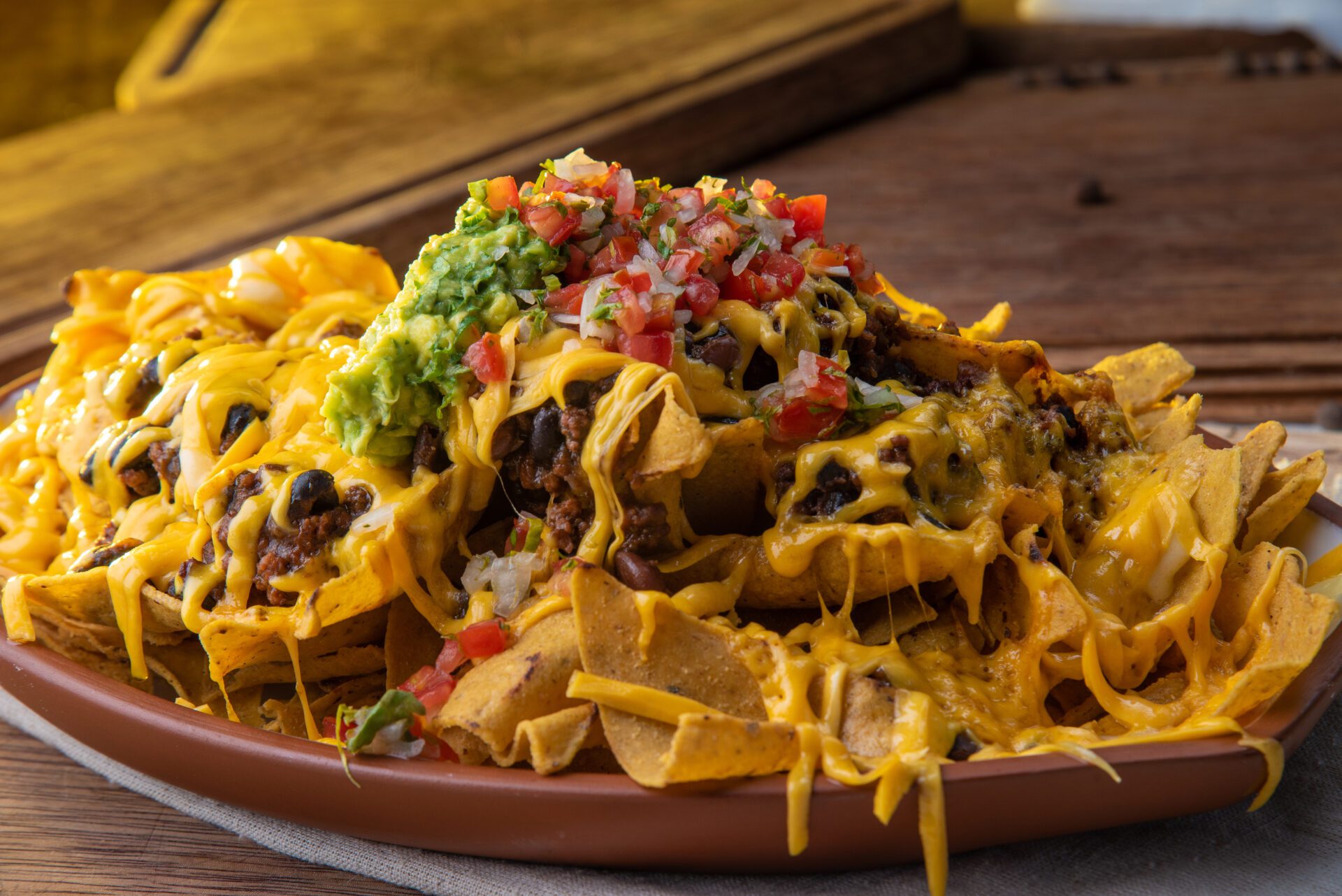 A plate of nachos with cheese, guacamole and tomatoes.